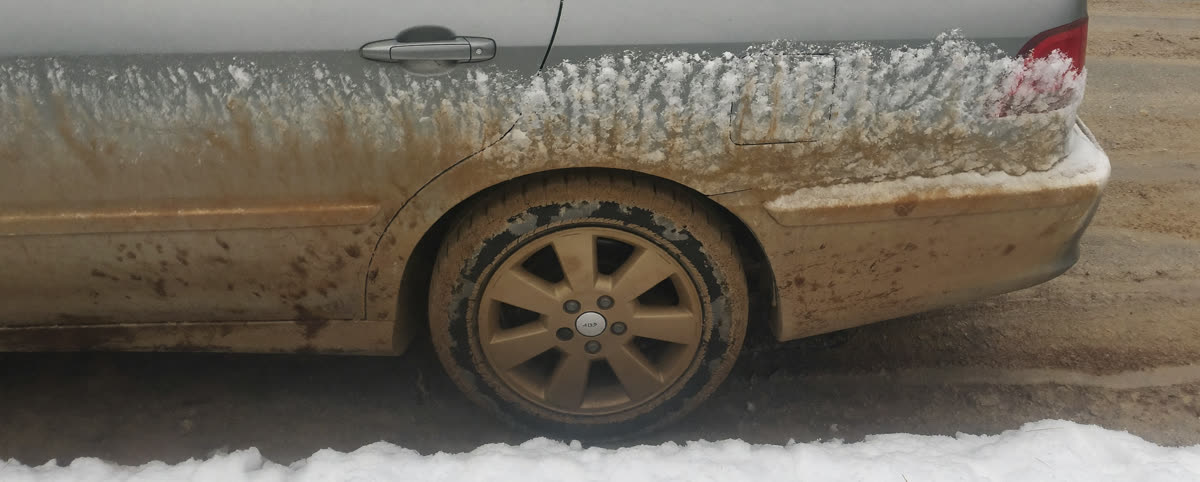 Road salt and slush caked onto a sedan's lower panel and wheel in an Alberta winter