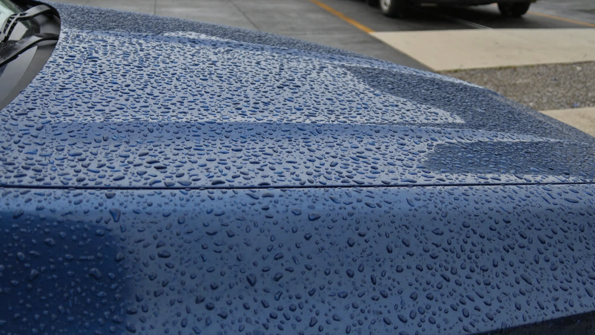 Water beading into tight droplets on freshly waxed dark blue car paint